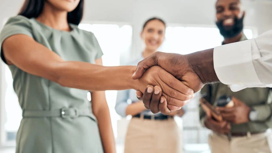 A Black man and a woman shake hands, with two blurred smiling people in the background.