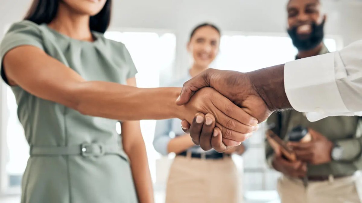 A Black man and a woman shake hands, with two blurred smiling people in the background.