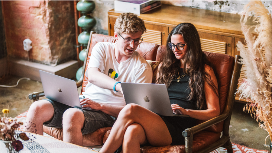 Two people sit on a sofa, each working on a laptop.