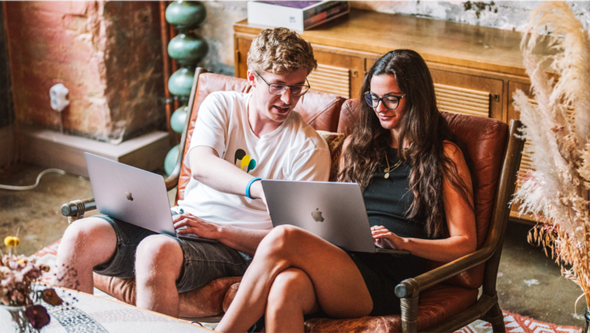 Two people sit on a sofa, each working on a laptop.