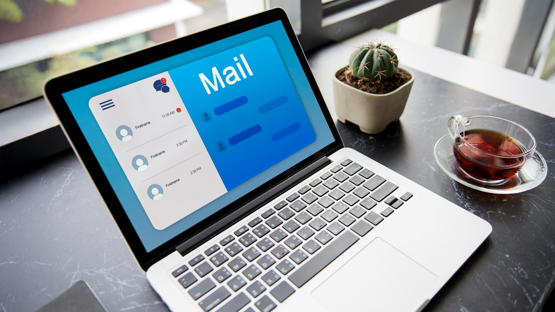 A laptop displaying a "Mail" application on a marble desk next to a cactus and a cup of tea.