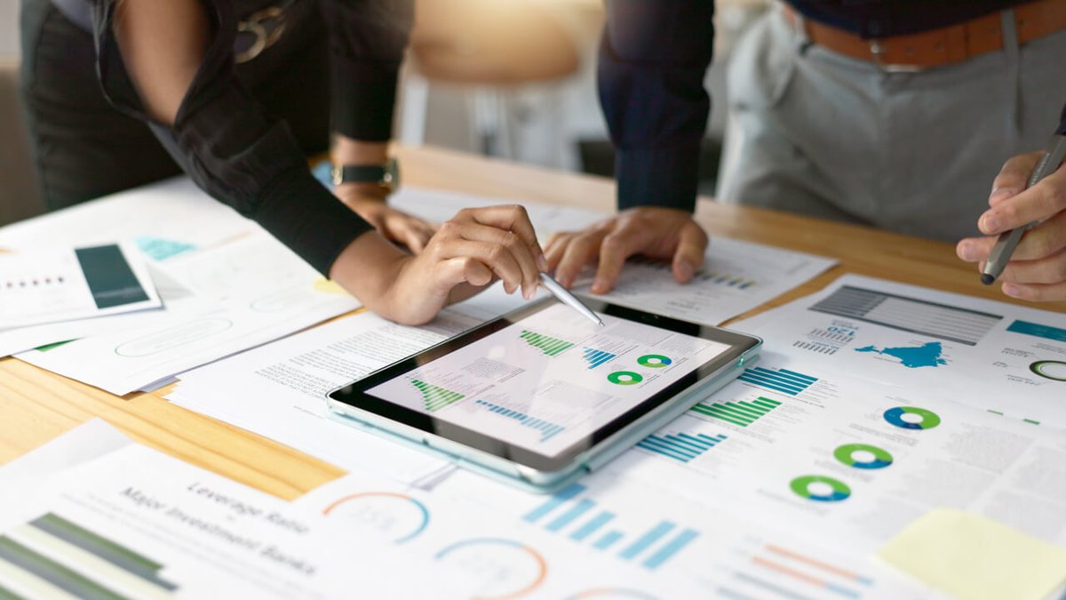 Two people analyzing charts and data on a tablet and paper documents.
