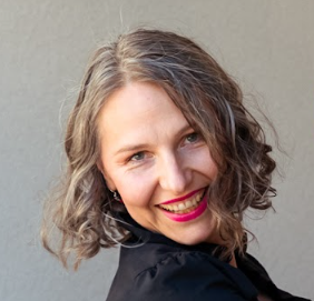 A smiling woman with grey hair and bright pink lipstick.