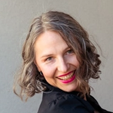 A smiling woman with grey hair and bright pink lipstick.