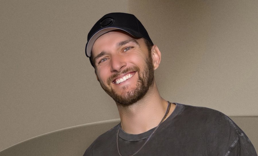 Un homme avec une barbe et une casquette de baseball noire sourit largement face à l'objectif.