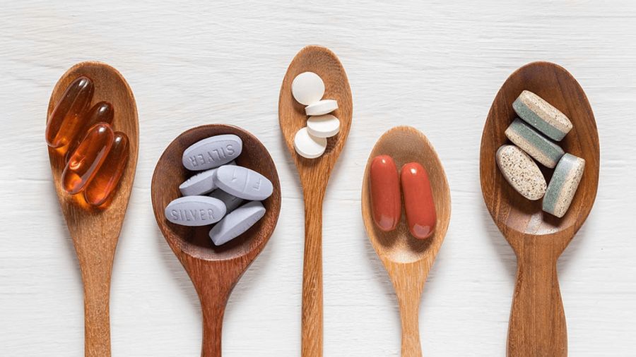 Five wooden spoons filled with various pills and supplements on a white surface.