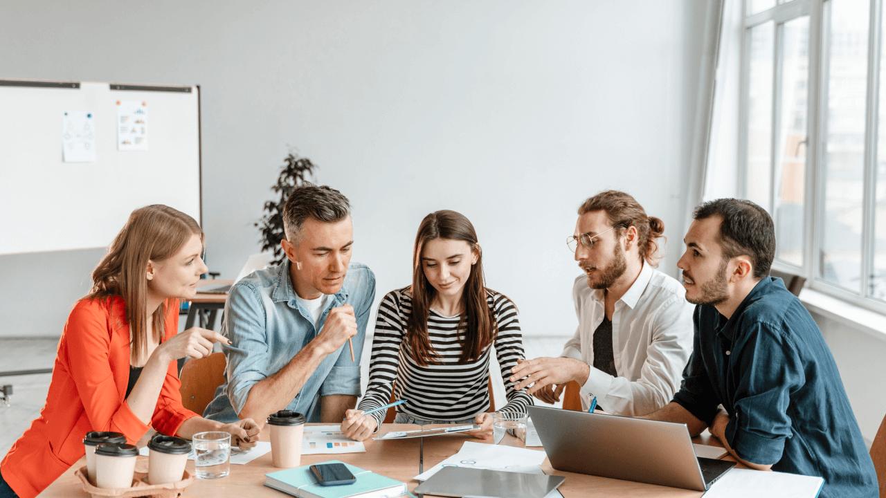 Five people in a bright office sitting around a table, discussing documents.