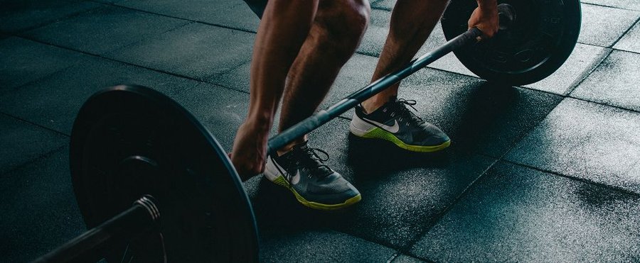 Person's legs and hands gripping a barbell on a gym floor.