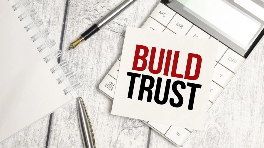 A sticky note reading "BUILD TRUST" on a calculator, notebook, and pens.