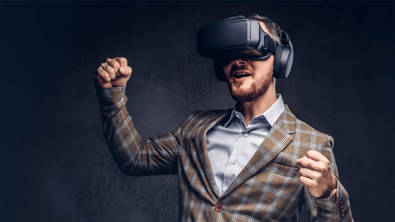 A man wearing a VR headset and headphones celebrates with clenched fists.