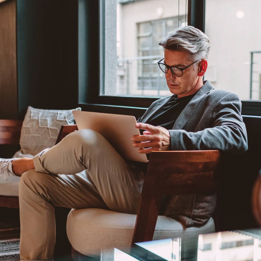 A focused man in a blue shirt and glasses looking down at a laptop.
