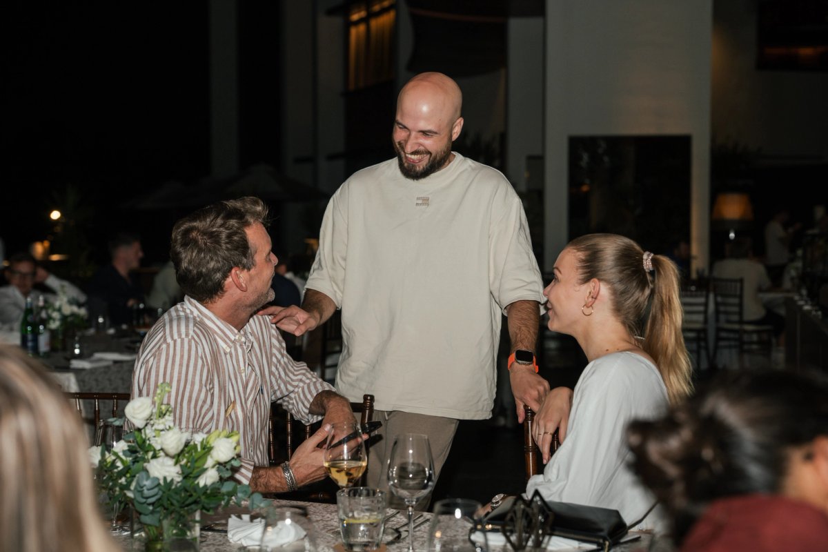 Three people smiling and conversing at an outdoor evening dinner.
