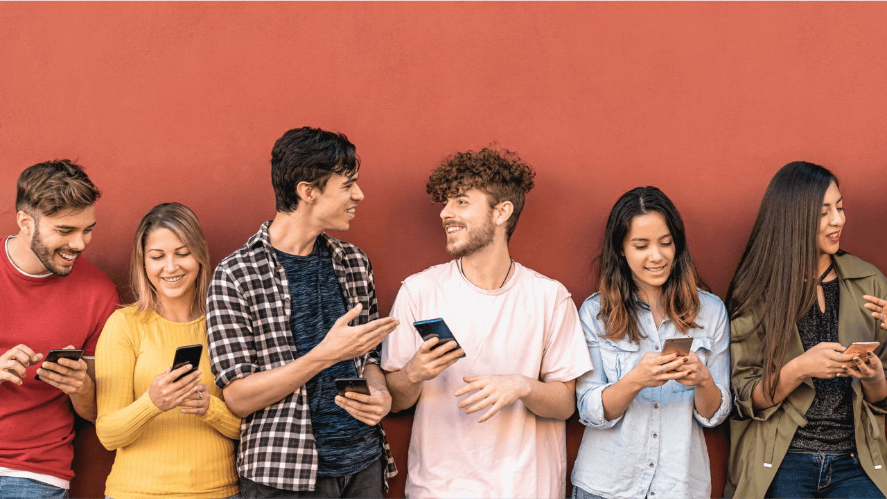 A group of young people using smartphones against a red wall.