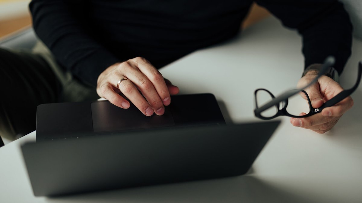 Hands on a laptop, one hand holding glasses.