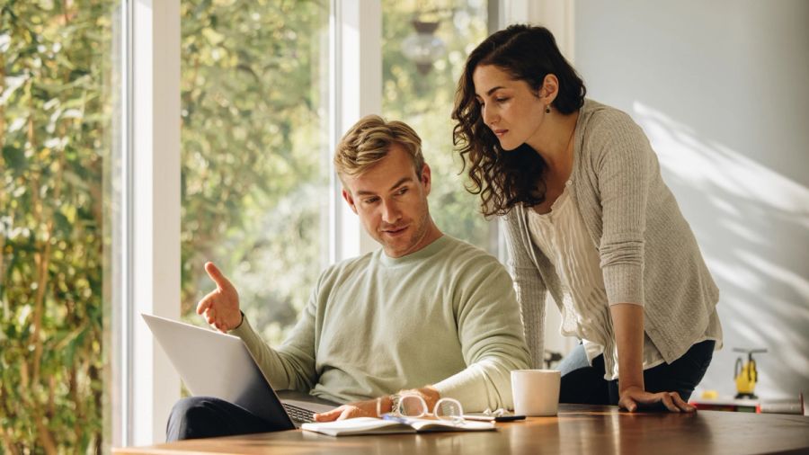 A man and woman looking at a laptop together, the man gesturing.