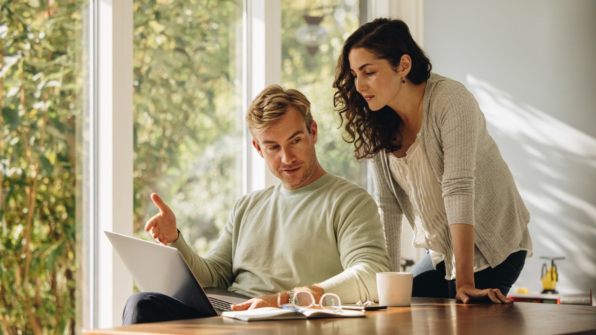 A man and woman looking at a laptop together, the man gesturing.