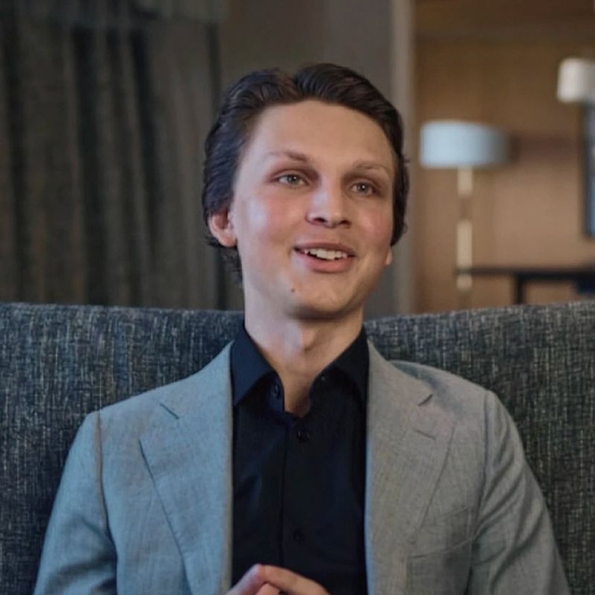 Young man in a grey suit and black shirt, smiling.