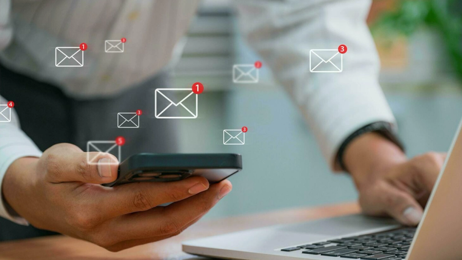 Floating email notifications surround hands using a smartphone and laptop.
