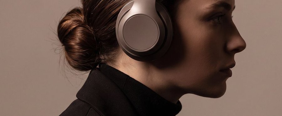 A woman in profile wearing light gray over-ear headphones and a dark top.