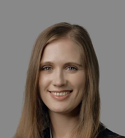 A smiling woman with long light brown hair against a grey background.