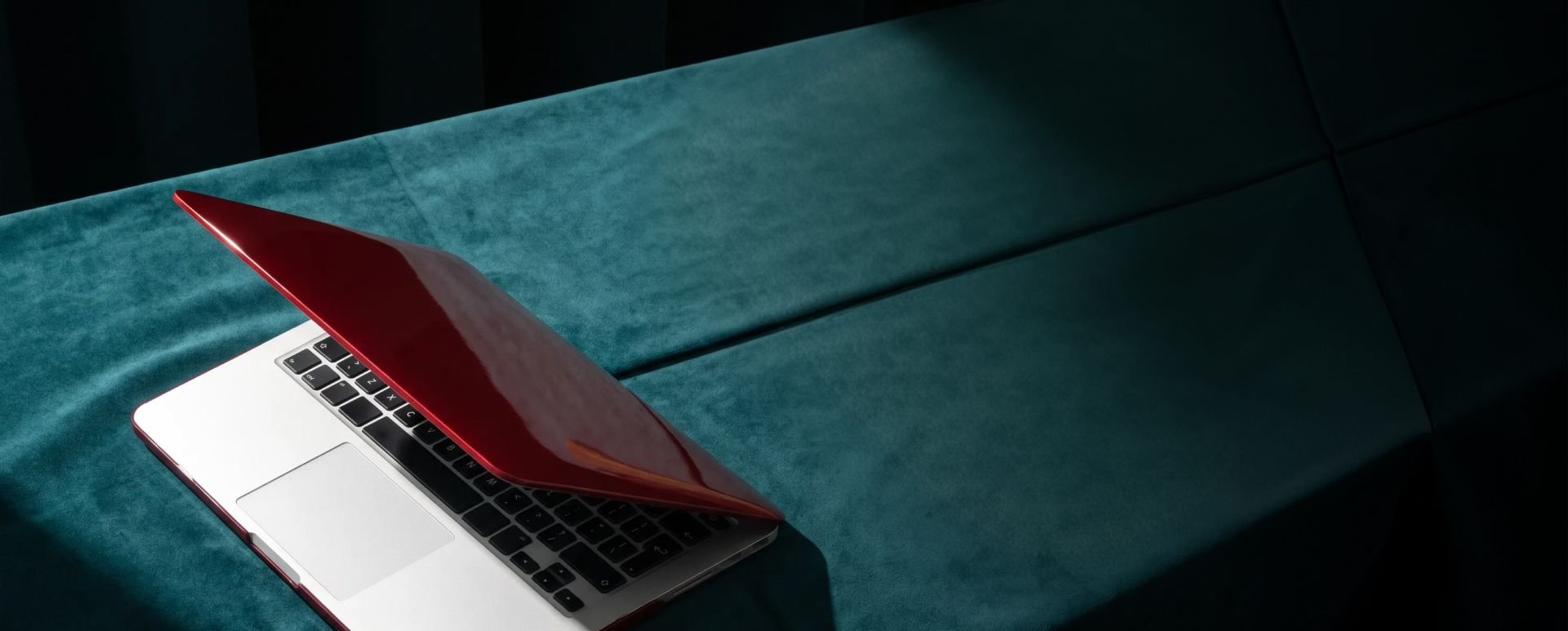 Red laptop on a teal velvet surface.