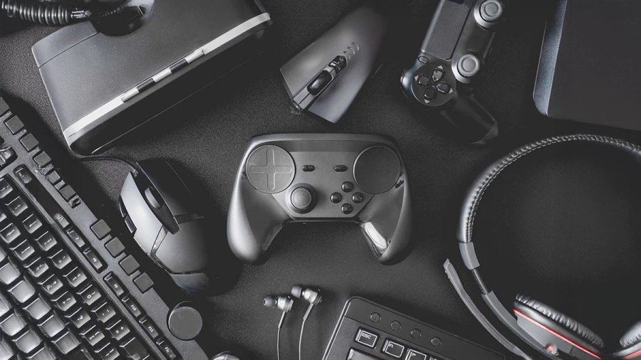 A flat lay of various black gaming peripherals including controllers, keyboard, mouse, headset, and VR headset.