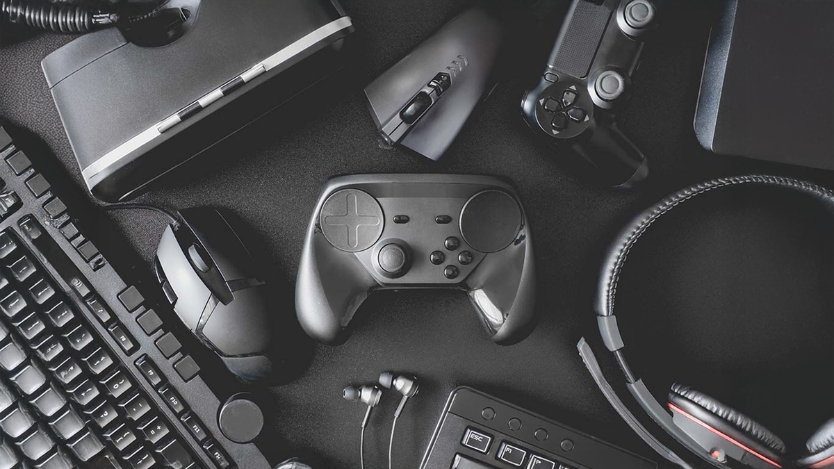 A flat lay of various black gaming peripherals including controllers, keyboard, mouse, headset, and VR headset.