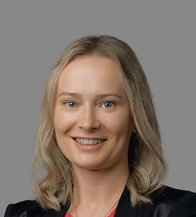 Headshot of a smiling blonde woman in a black blazer against a gray background.