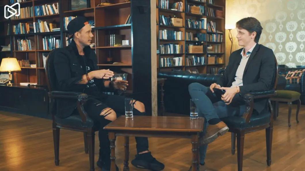 Two men sitting at a table in a library, engaged in conversation.