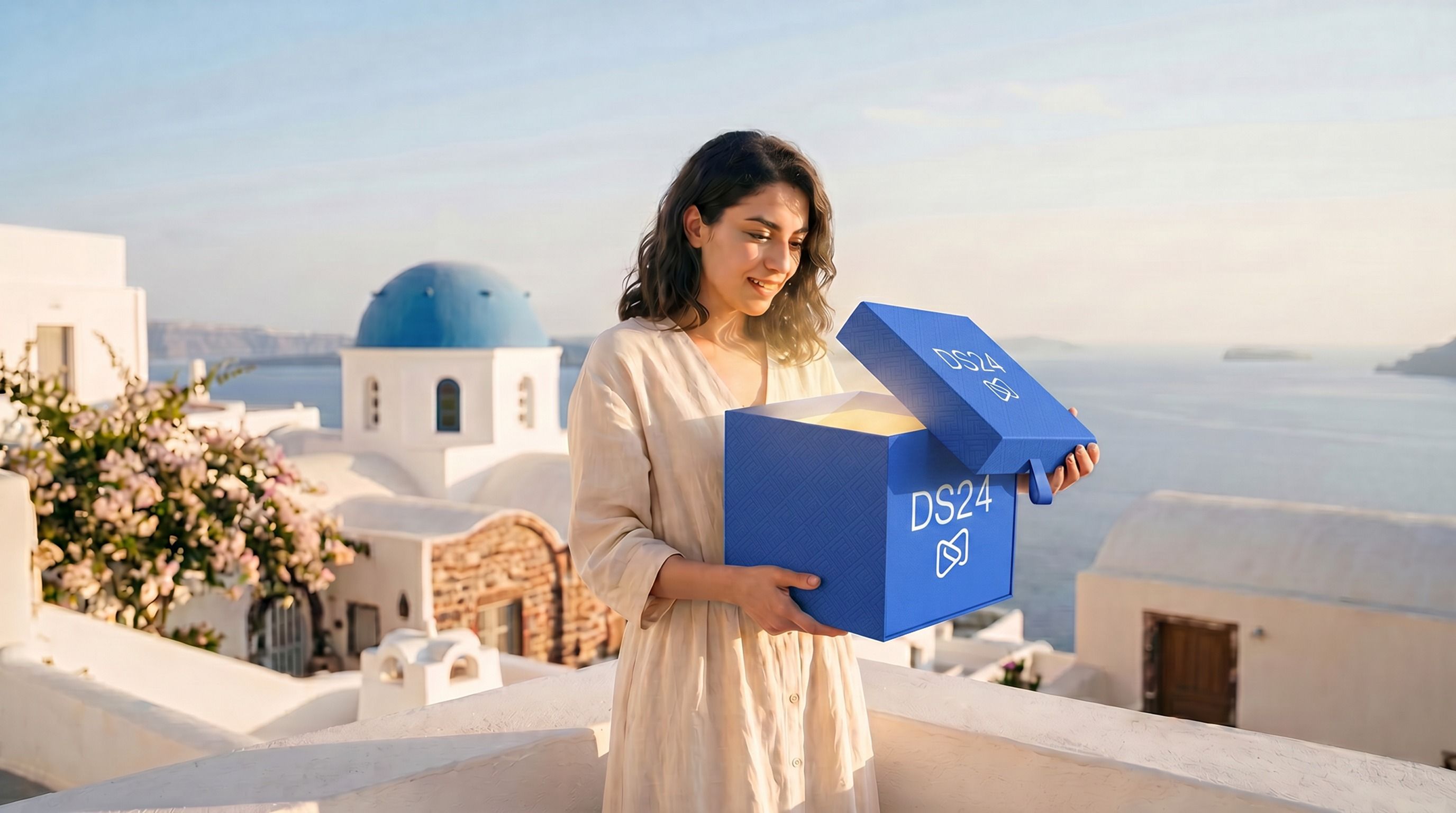 A smiling woman looks into an open, glowing blue box marked "DS24" in a scenic coastal town with white buildings and a blue dome.