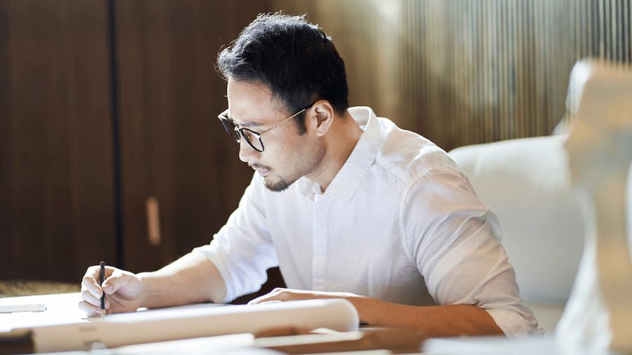 A man in a white shirt and glasses draws on paper.