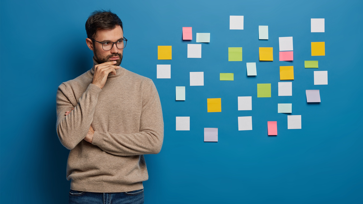 A thoughtful man gazes at colorful sticky notes on a blue wall.