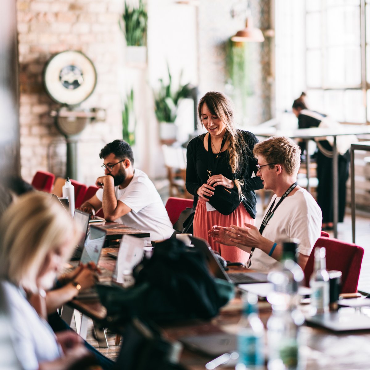 People working on laptops and chatting at a long table in a modern co-working space.