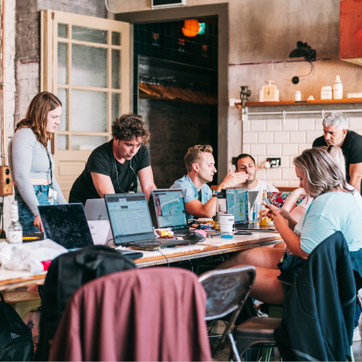 A diverse group of people collaborating around laptops at a long table.