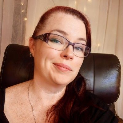 A woman with reddish-brown hair and glasses smiles softly.