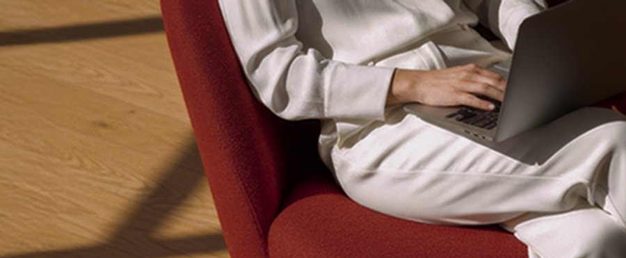 Person in white clothing typing on a laptop while sitting in a red chair.