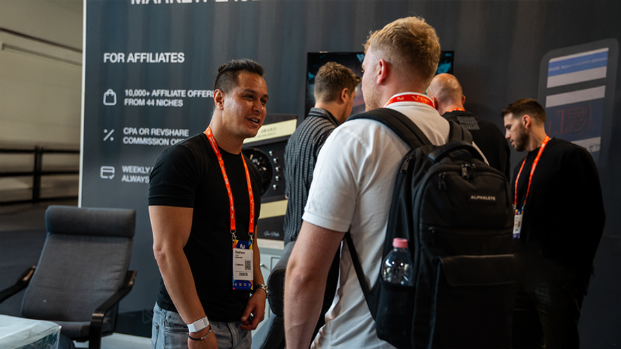 Two men talking at a conference booth with an "FOR AFFILIATES" banner.