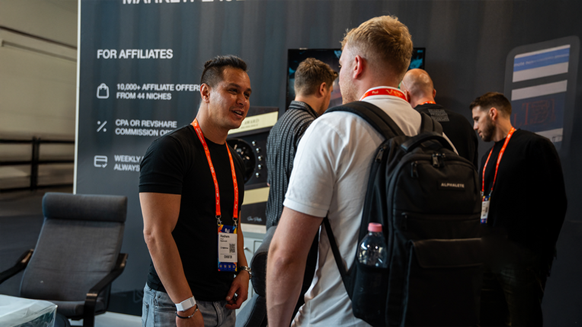 Two men talking at a conference booth with an "FOR AFFILIATES" banner.