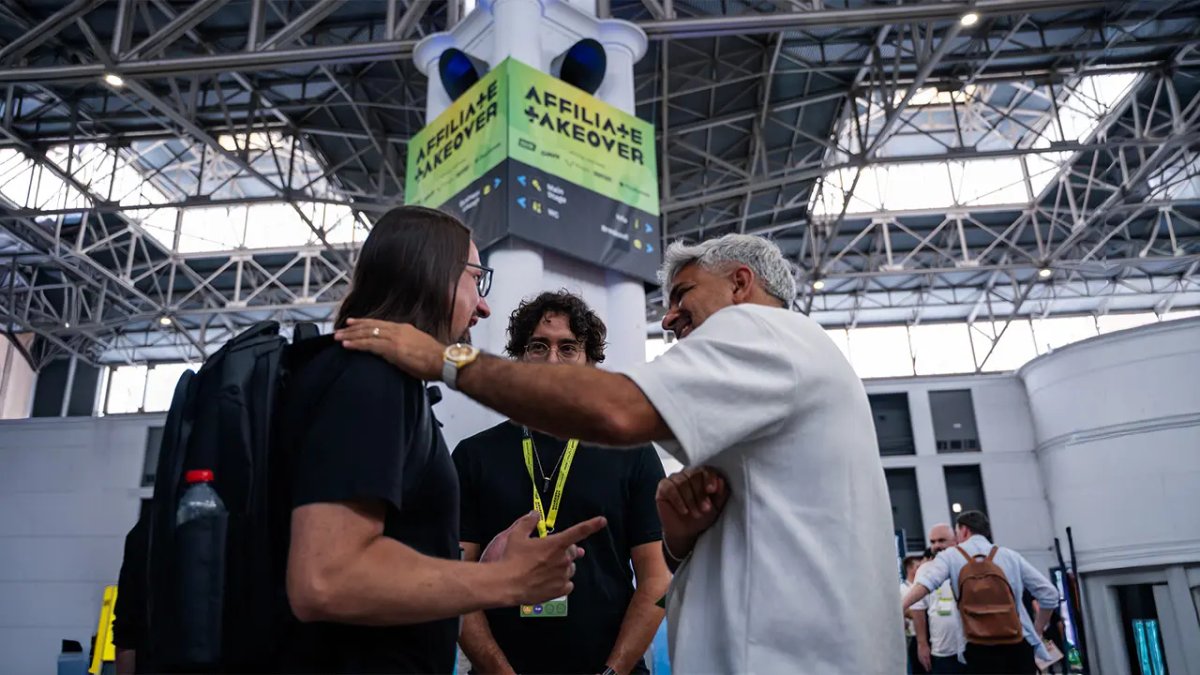 Two men conversing at an event, one with a hand on the other's shoulder, beneath an "AFFILIATE + TAKEOVER" banner.