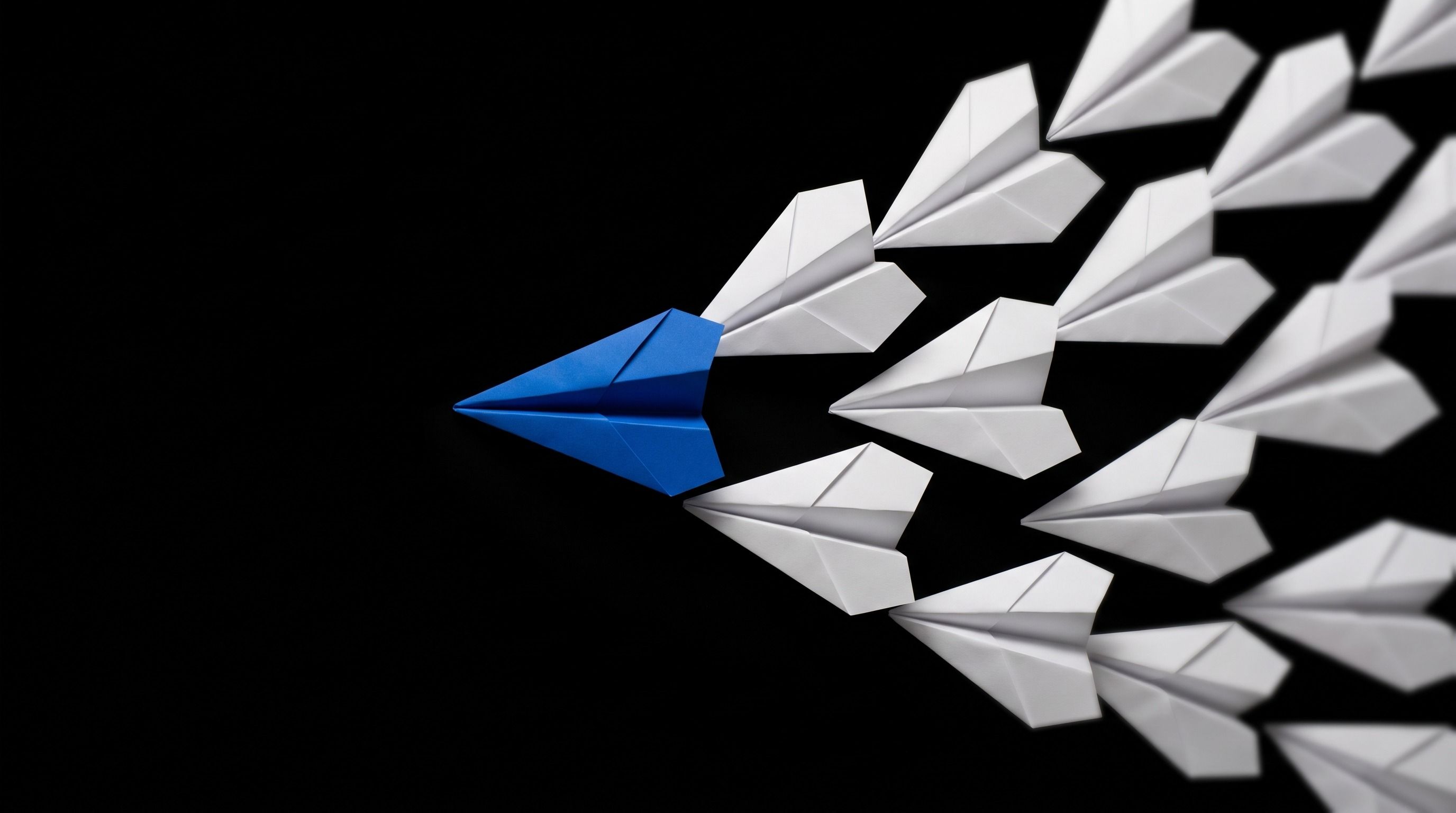 A blue paper airplane leads a V-formation of white paper airplanes on a black background.