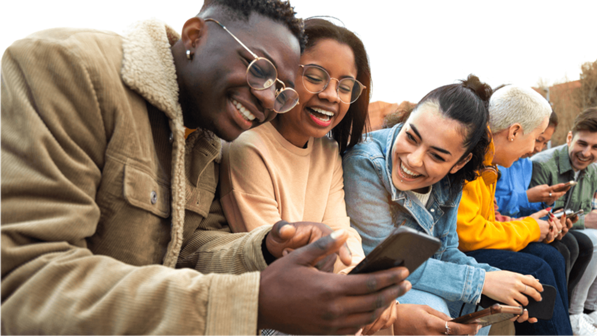Diverse young adults laughing and looking at smartphones.