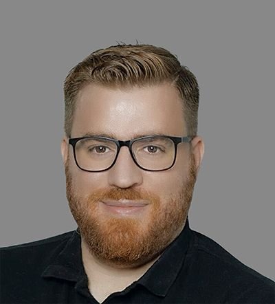 Headshot of a man with reddish-brown hair, ginger beard, and black-rimmed glasses smiling.
