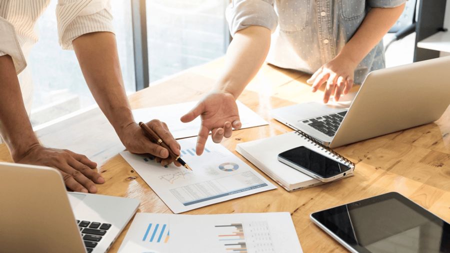Two people collaborating over business documents with charts and laptops on a table.