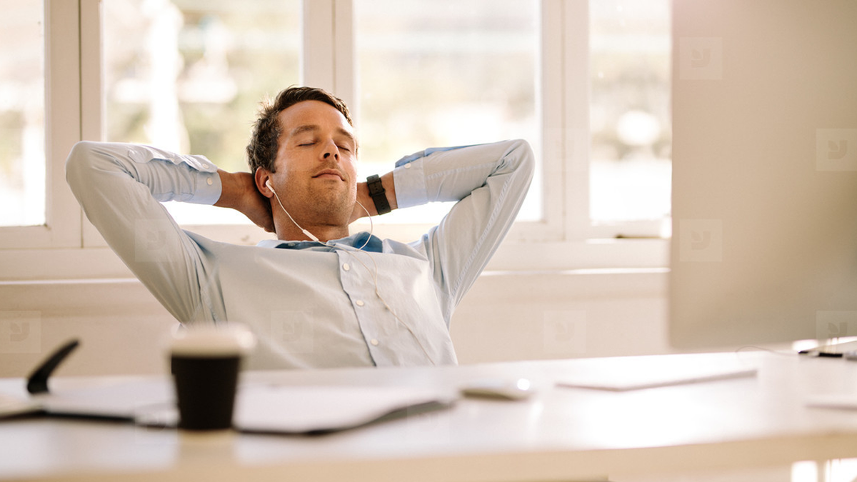 Man with earbuds relaxing in a chair with eyes closed and hands behind his head.