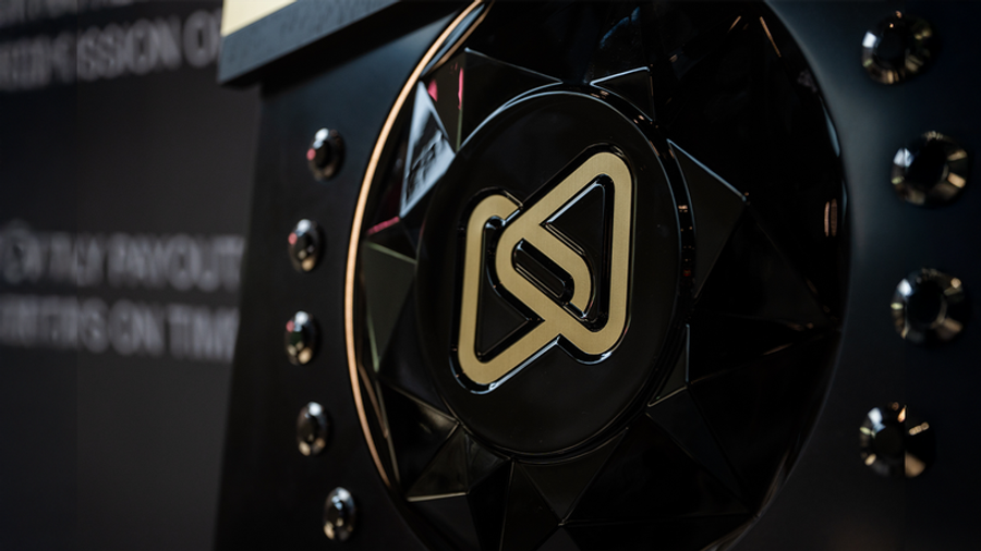 A black trophy or award with a gold intertwined 'S' logo on a faceted surface.