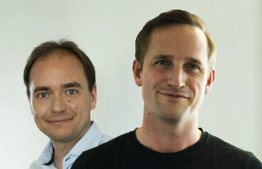 Two smiling men, one in a black t-shirt and one in a light blue shirt.