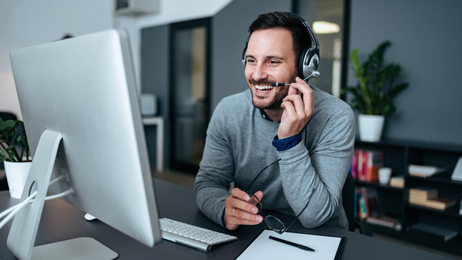 Smiling man with a headset at a computer.
