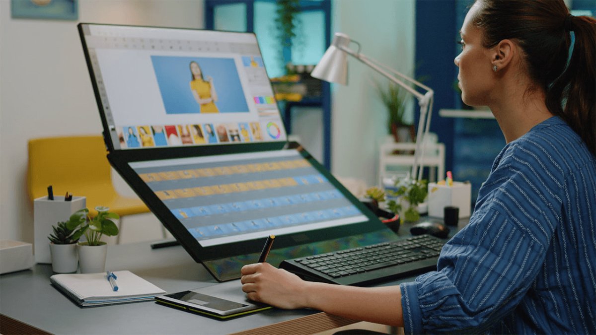 A woman using a stylus and graphics tablet to edit photos on a large, tilted monitor.