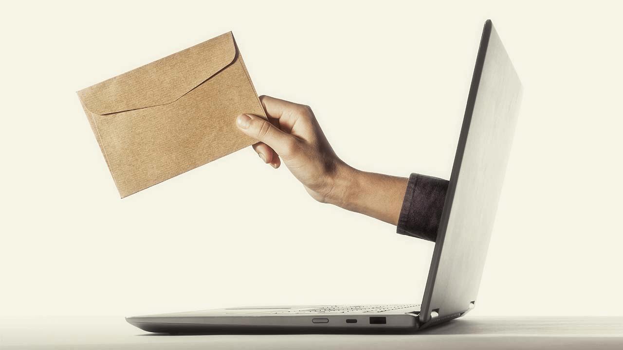 A hand emerges from a laptop screen, holding a brown envelope.