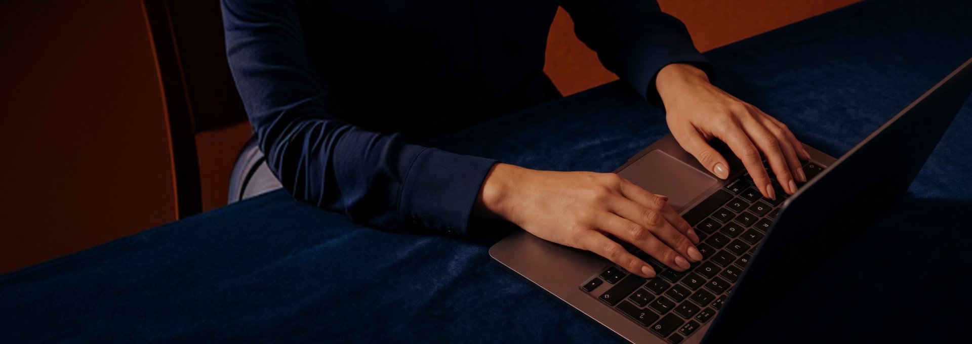 Person's hands typing on a laptop placed on a dark blue surface.